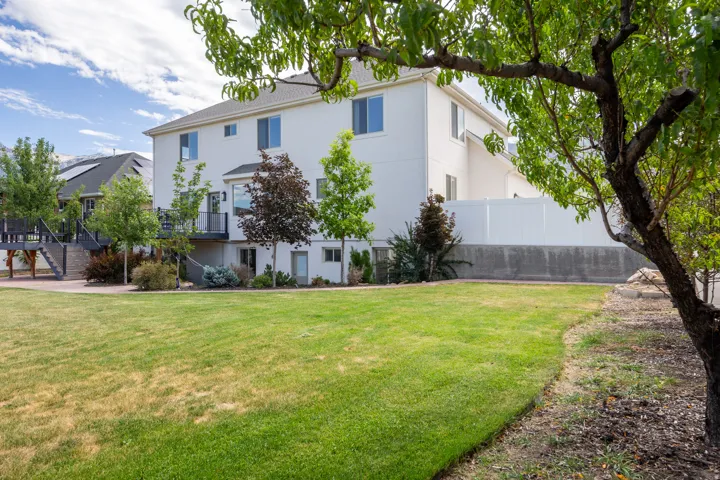 Spacious backyard featuring a large green lawn, mature trees, and a white privacy fence