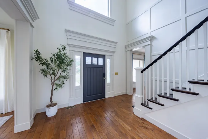 Entry foyer featuring wood-finish flooring, a dark-paneled door with sidelights, and a grand staircase with dark treads and white risers