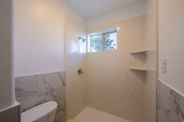 Walk-in shower featuring a chrome showerhead, a recessed window, and two corner storage shelves
