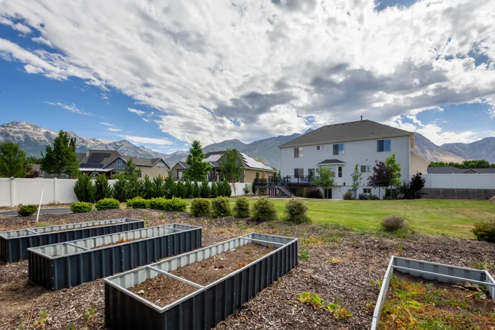 Expansive backyard featuring multiple raised garden beds, a spacious lawn area, and a white privacy fence