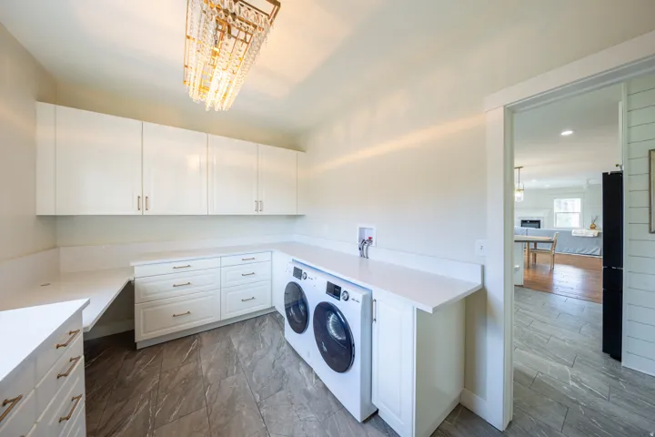 Dedicated laundry area featuring a modern chandelier, extensive white cabinetry, light-toned countertops, and durable tile flooring