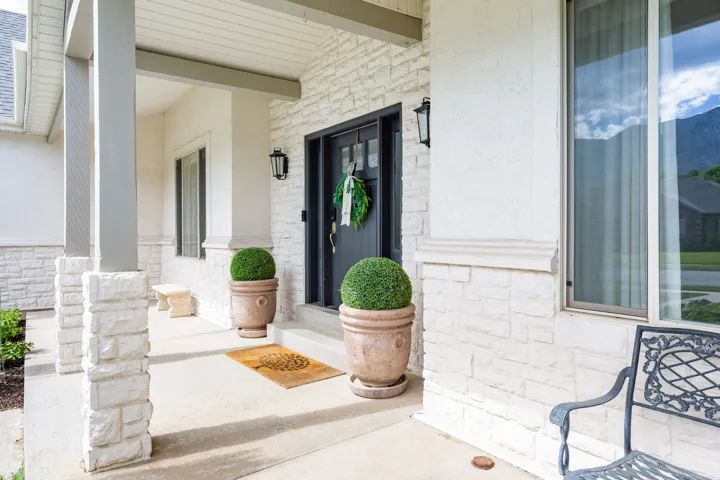 Front entry featuring a dark-paneled door with opaque glass details, white stacked stone veneer, textured stucco siding, and a covered porch with stone-clad columns