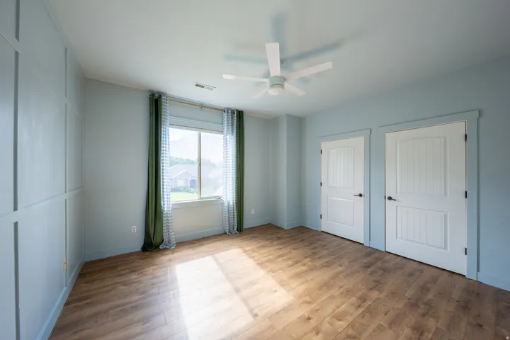Spacious interior room featuring wood-finish flooring, a ceiling fan, and a large window