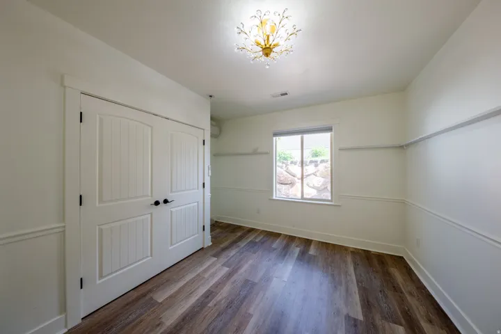 Spacious room featuring wood-finish flooring, white paneled double closet doors, and decorative wainscoting
