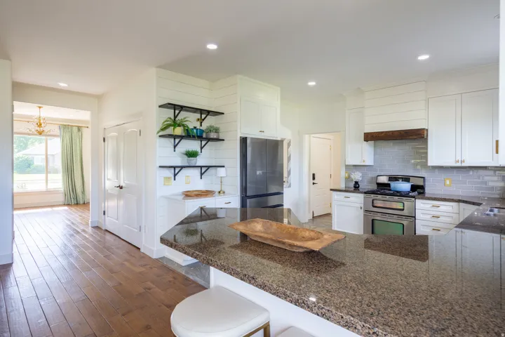 Kitchen featuring an expansive island with a granite-style countertop, stainless steel appliances, white cabinetry with gold-tone hardware, a subway tile backsplash, and wood-finish flooring