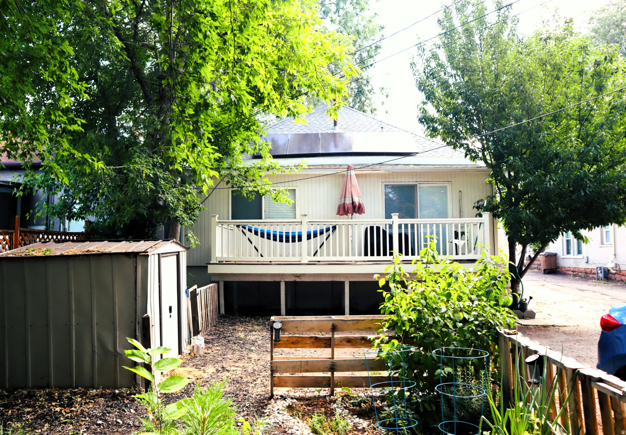 Rear exterior featuring a raised deck with white railing, sliding glass door access, and a metal storage shed