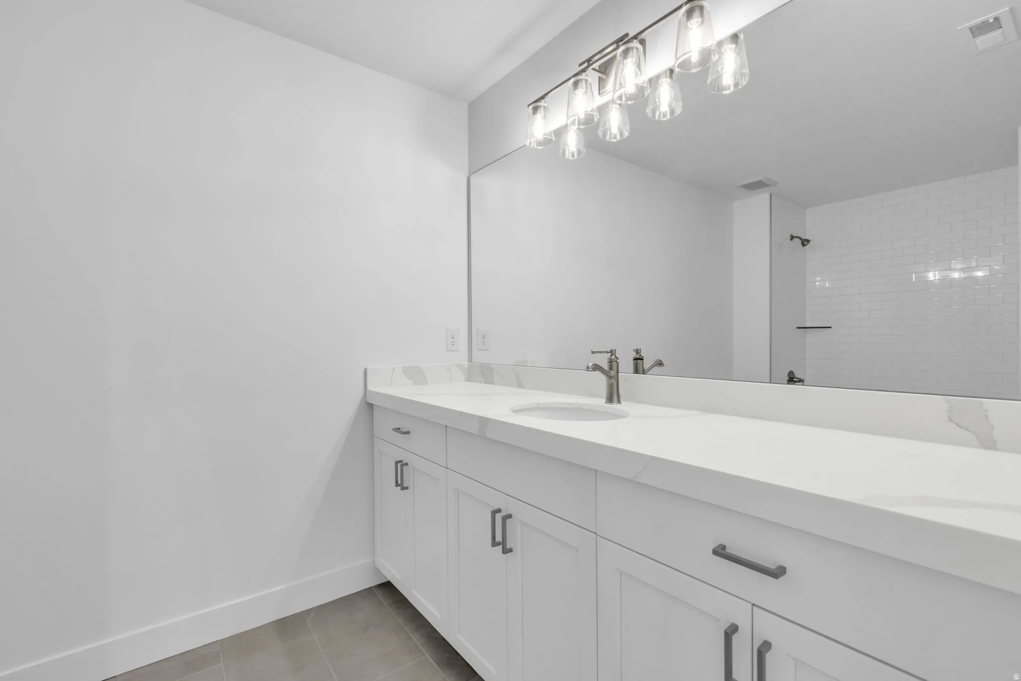 Large secondary bathroom with quartz countertop, and white shaker-style cabinetry with black hardware.