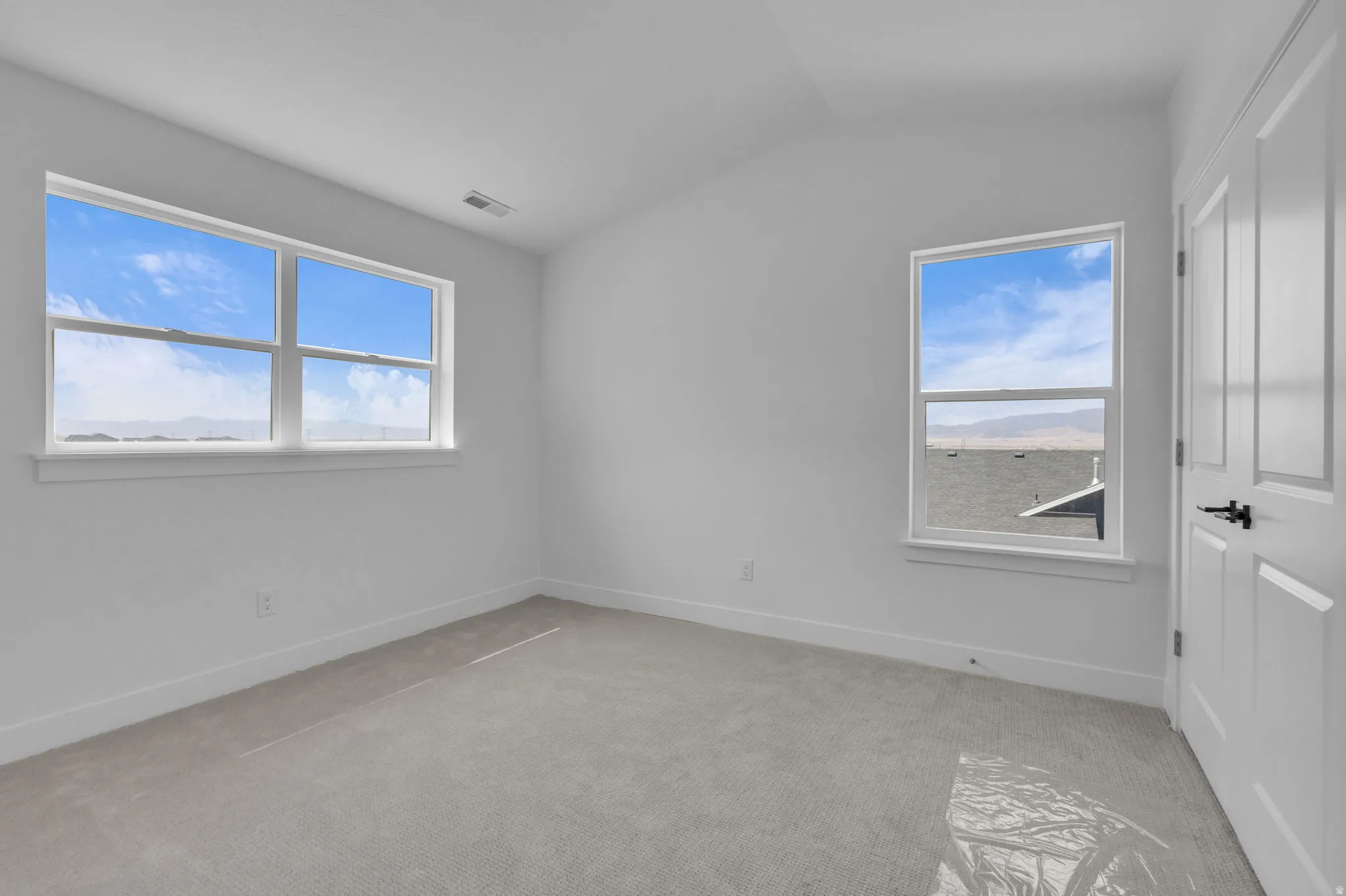 Vaulted bedroom #2 featuring two windows, neutral carpet, white walls, white trim, and white paneled double closet doors with matte black hardware.