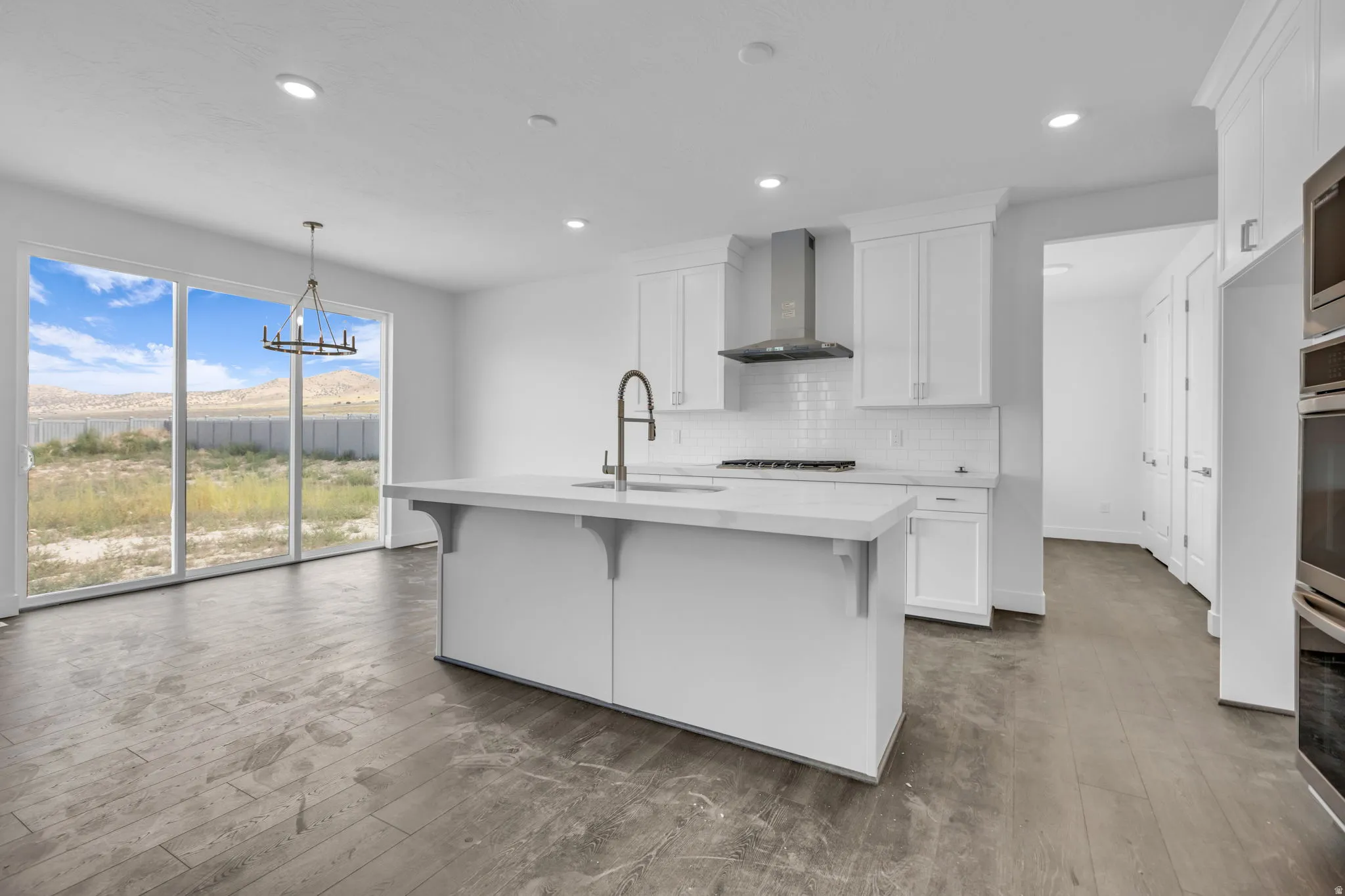 Large kitchen featuring a central island with an integrated sink, white cabinetry, and stainless steel upgraded appliances, including gas cooktop and double ovens.