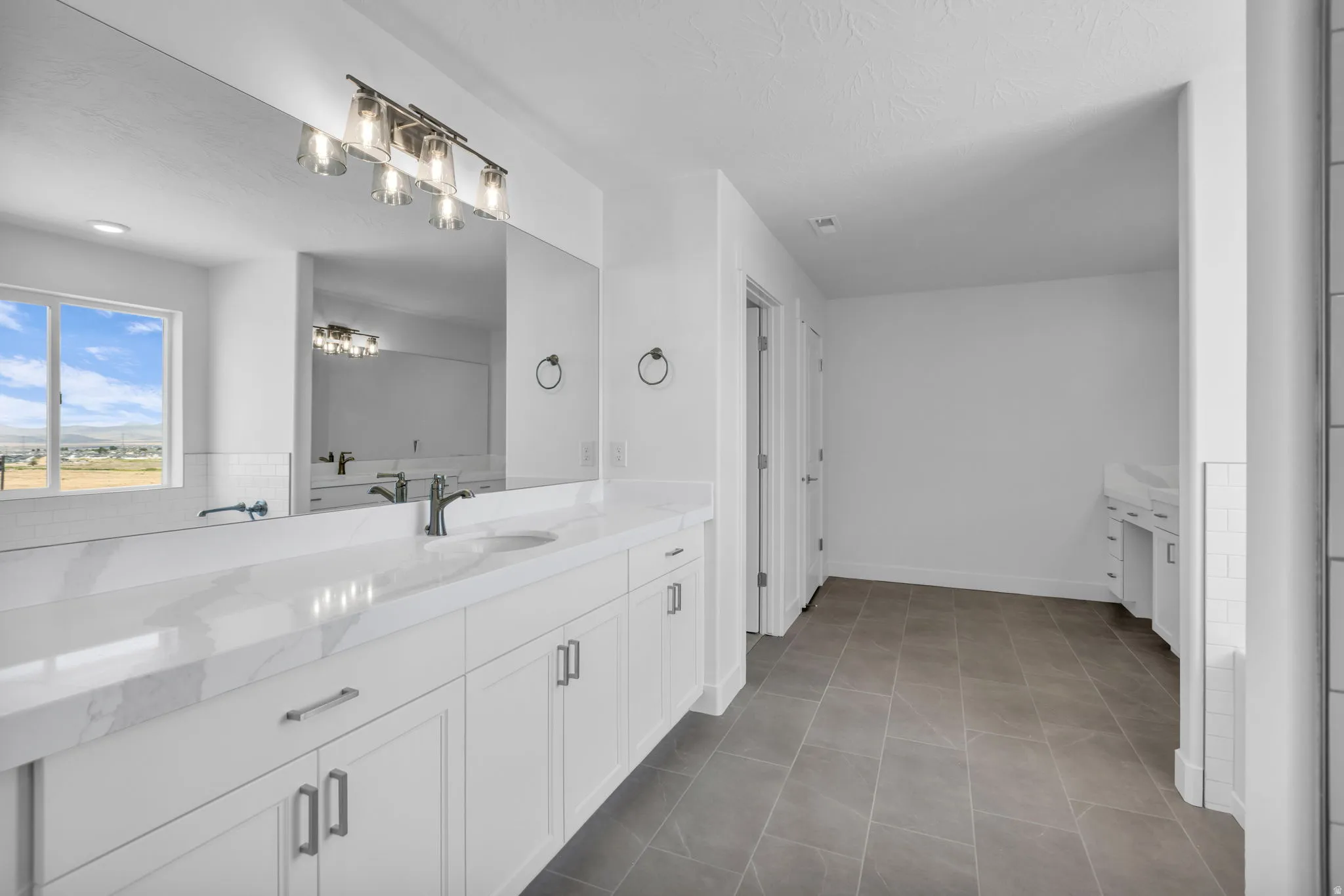 Spacious bathroom featuring a double vanity with white cabinetry, Quartz countertops, and separate sitting vanity, large tiled shower, soaker tub and entrance to an extremely large primary closet.