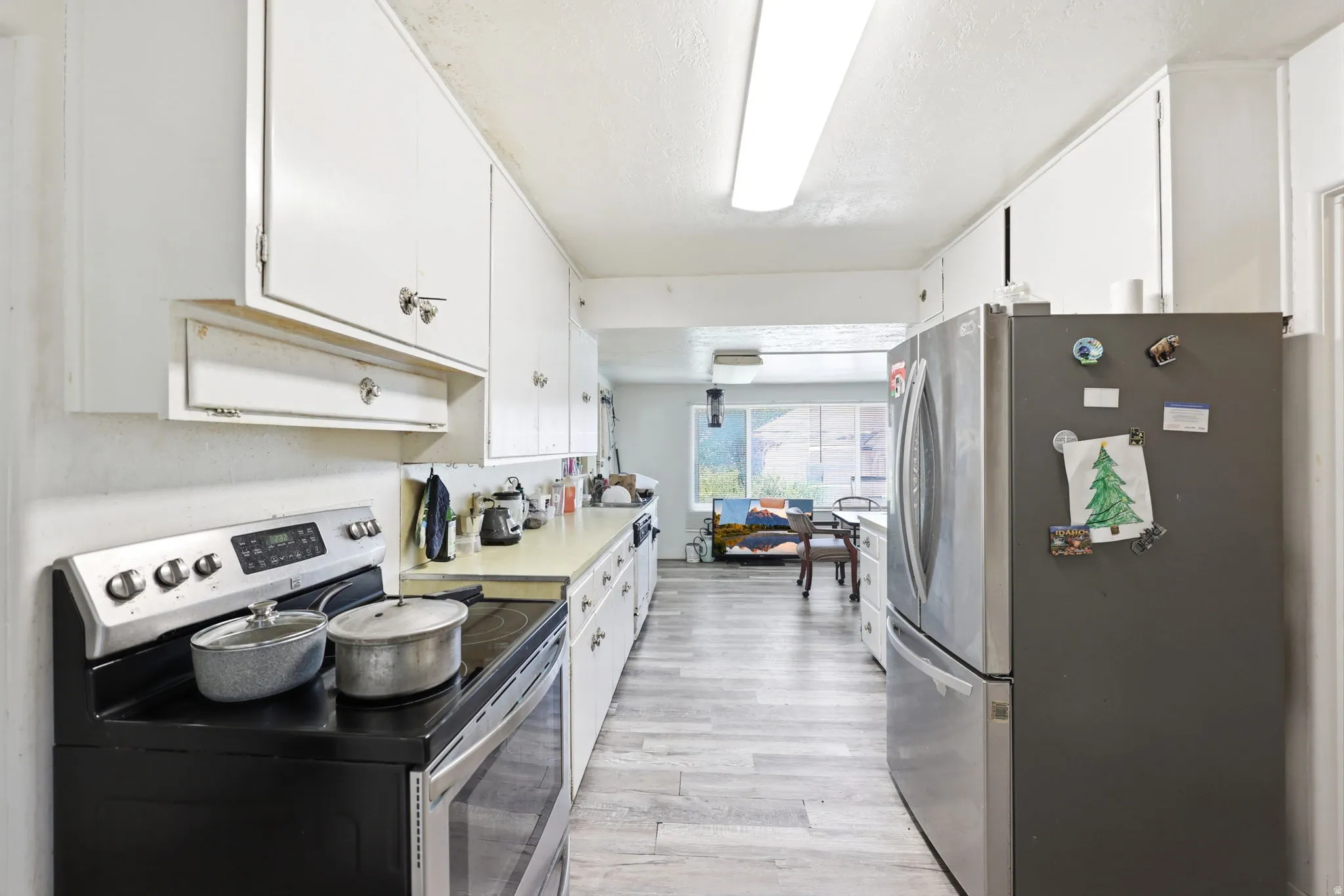 Galley kitchen featuring white cabinetry, light-toned countertops, and wood-finish flooring