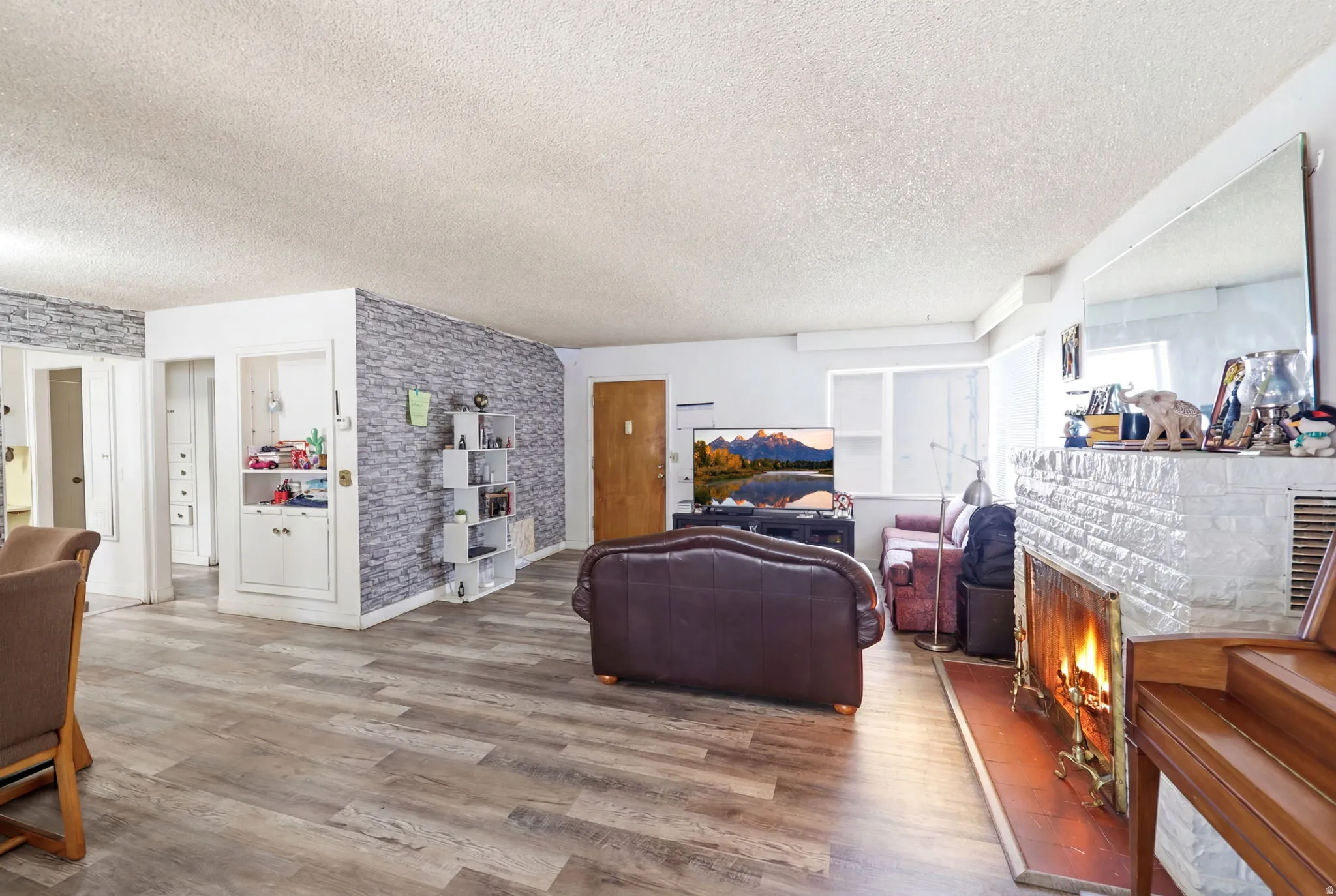 Spacious living area featuring wood-finish flooring, a white brick fireplace with a hearth, and a built-in display cabinet