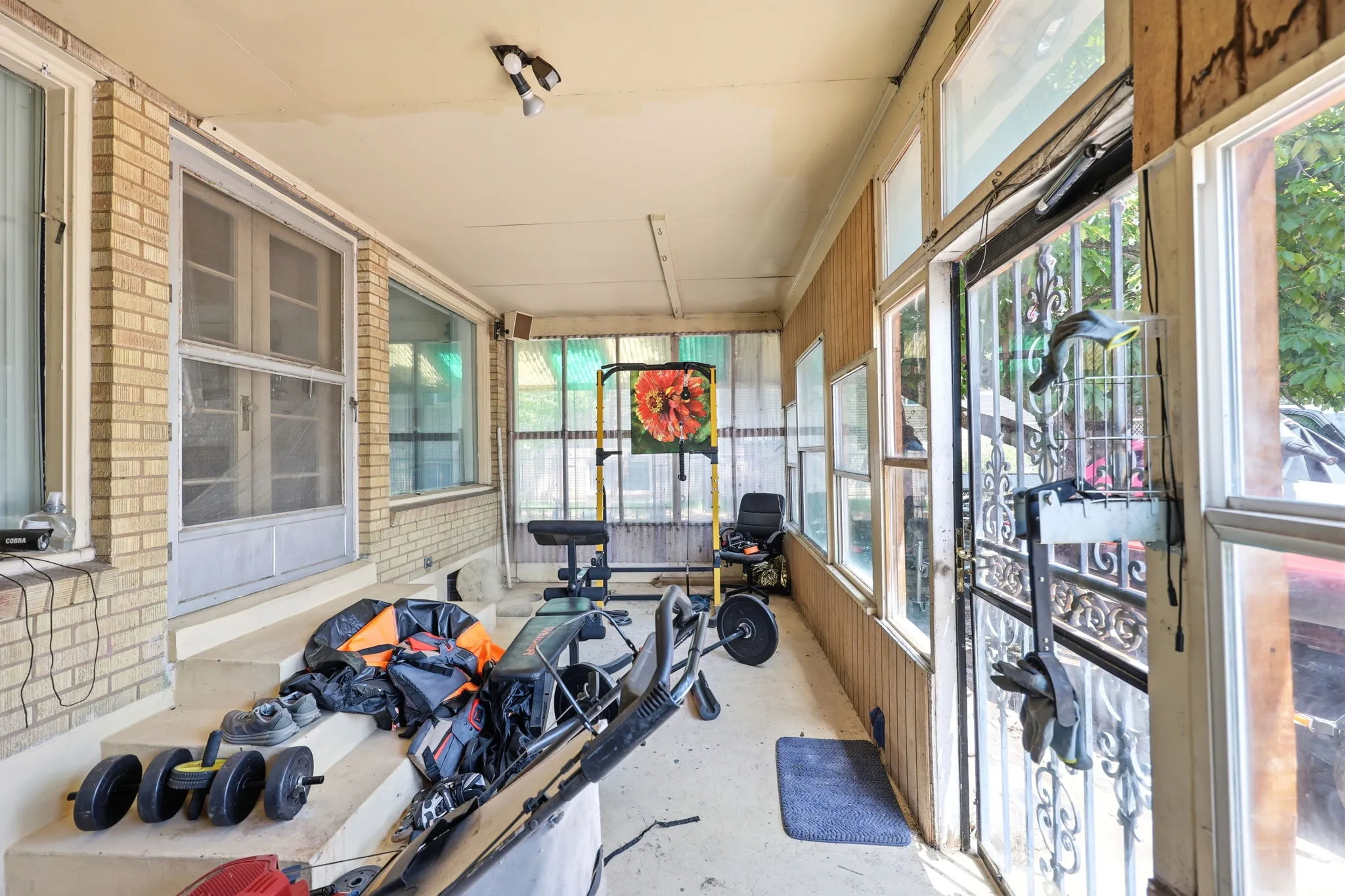 Enclosed porch featuring a brick exterior wall, multiple windows, a screened entry door, and a security door with ornate metalwork