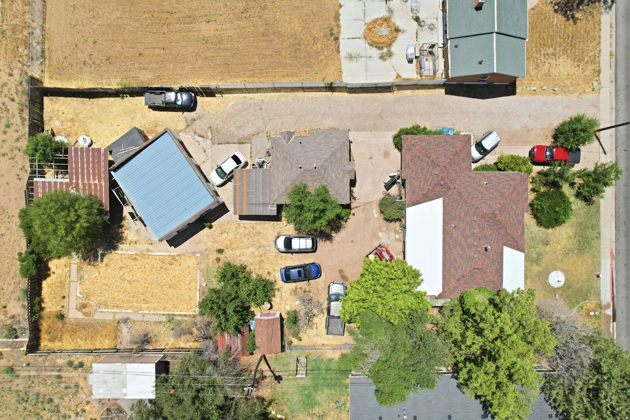 Aerial perspective showcasing two primary structures on a large lot, featuring a brown shingle roof on the main dwelling and a blue metal roof on an auxiliary building