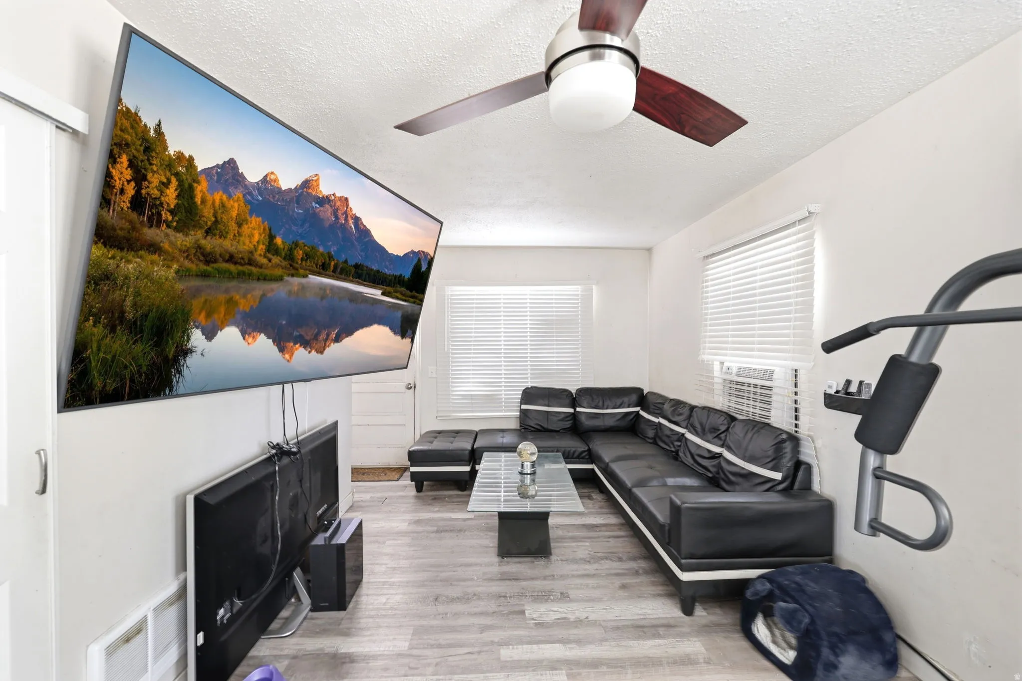 Living area featuring wood-finish flooring, white walls, and a ceiling fan with integrated lighting