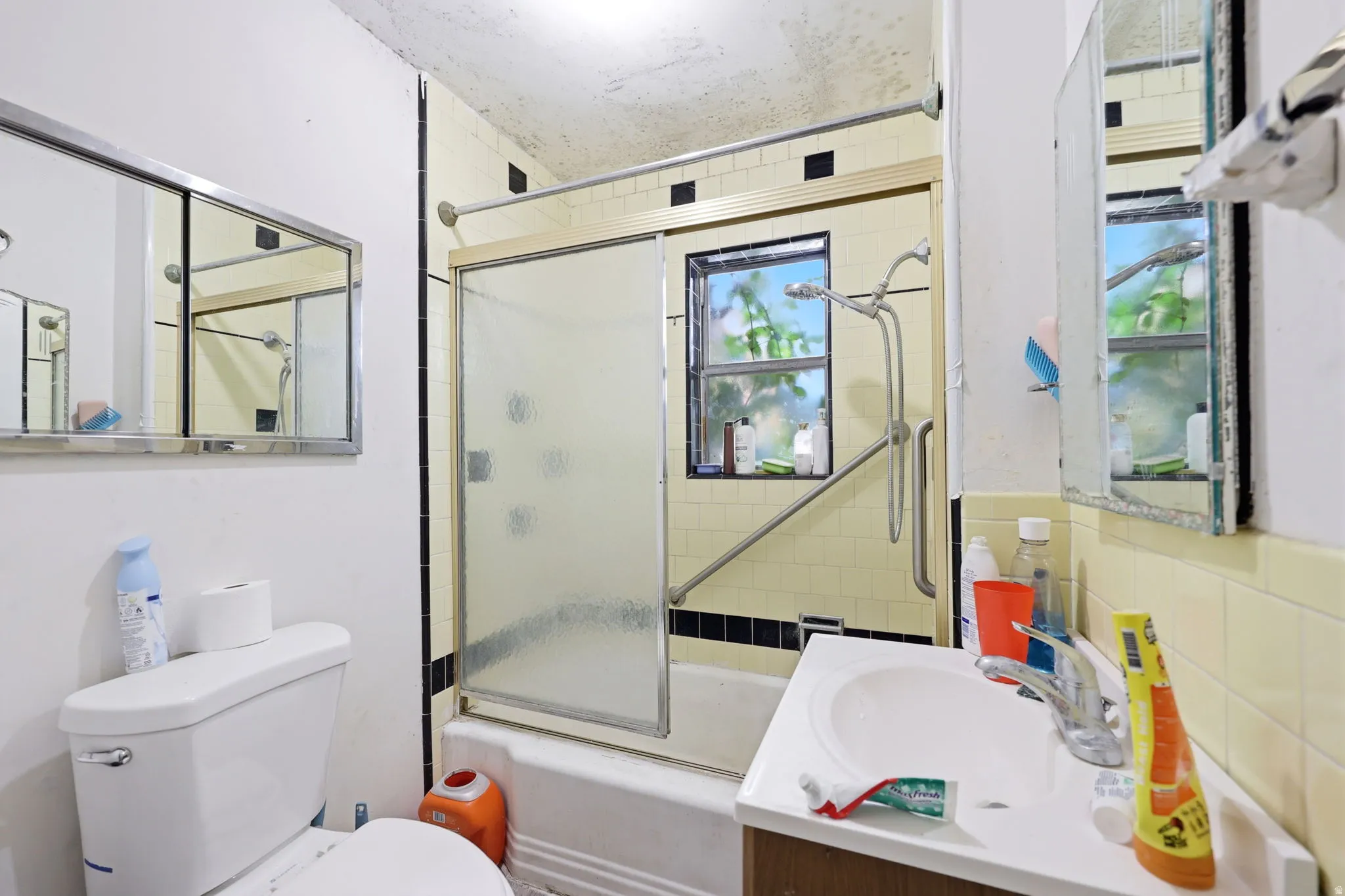 Bathroom featuring a toilet, a single vanity with a basin sink, and a shower-over-tub with a sliding glass door