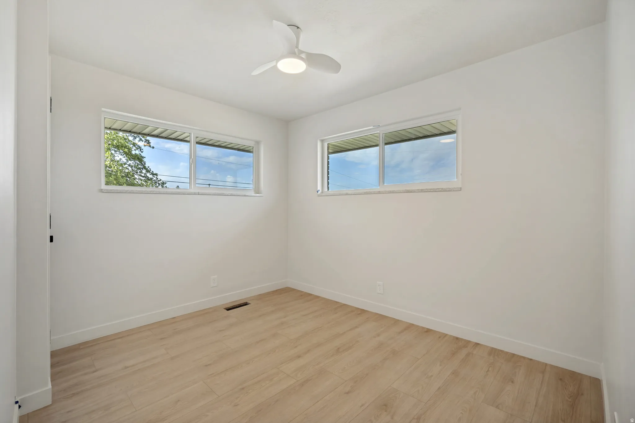 Bright interior space featuring wood-finish flooring, white walls, and a contemporary ceiling fan with integrated lighting