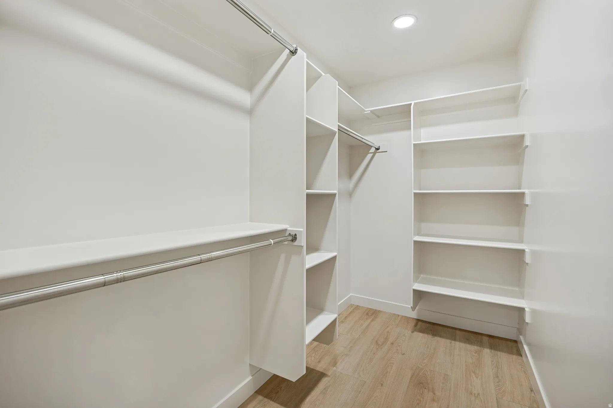 Walk-in closet featuring light wood-finish flooring, recessed lighting, white built-in shelving, and multiple clothing rods