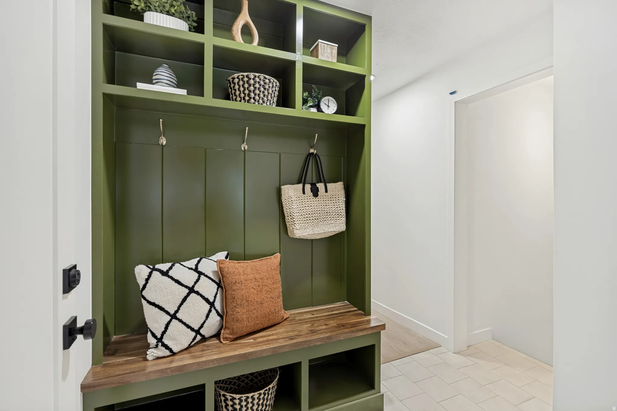 Built-in entryway storage featuring a custom green finish, natural wood bench, integrated shelving, and metal hooks