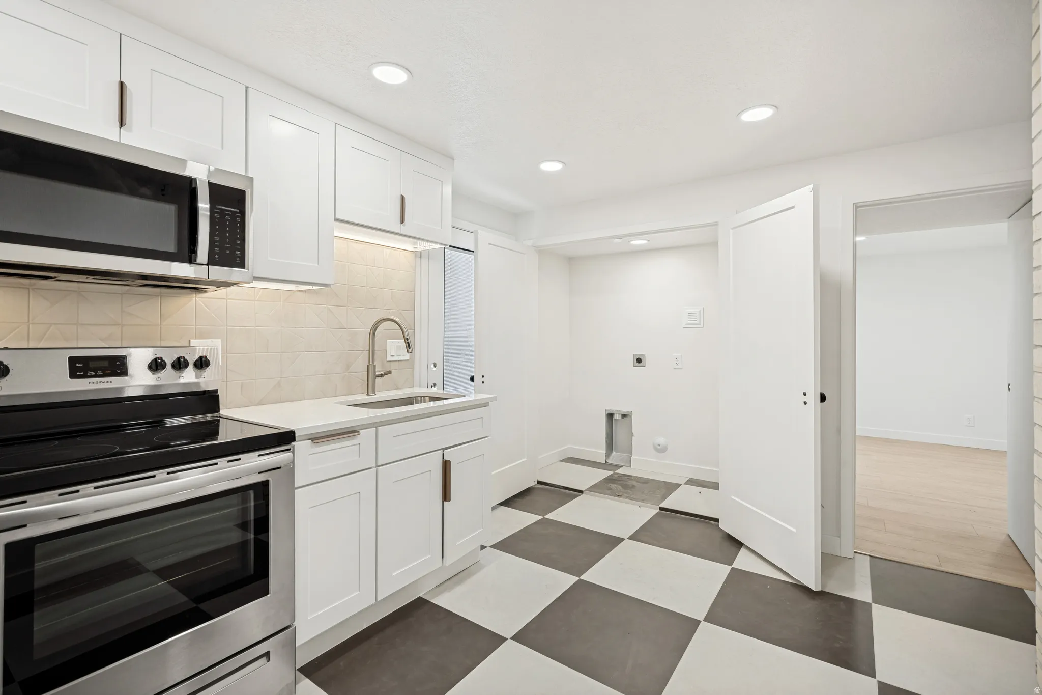 Kitchenette featuring stainless steel appliances, white cabinetry with bronze hardware, a light-toned tile backsplash, and a checkered floor