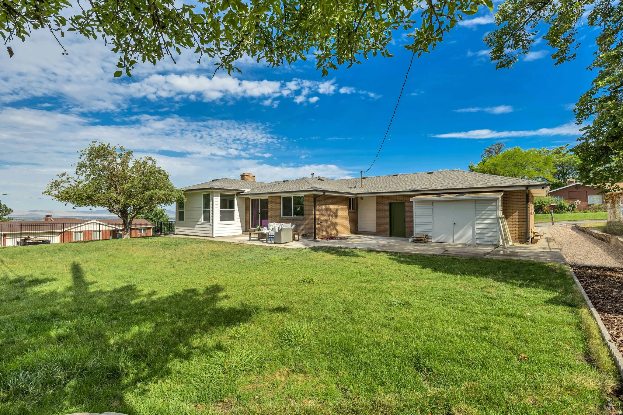 Expansive green lawn surrounds the property, featuring a concrete patio and sunroom extension with multiple windows