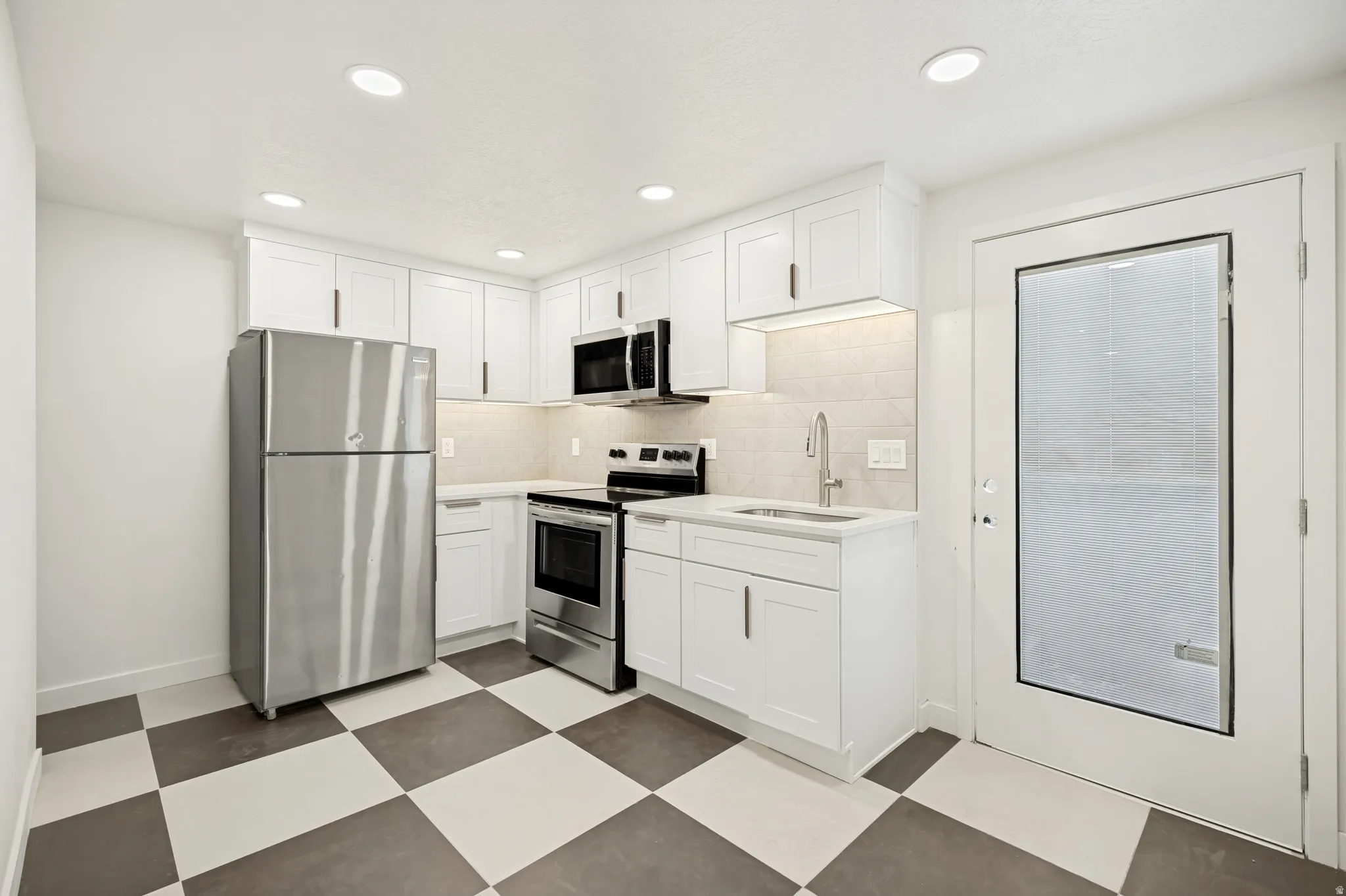 Modern kitchen featuring white shaker cabinetry, stainless steel appliances, a checkerboard tile floor, and recessed lighting