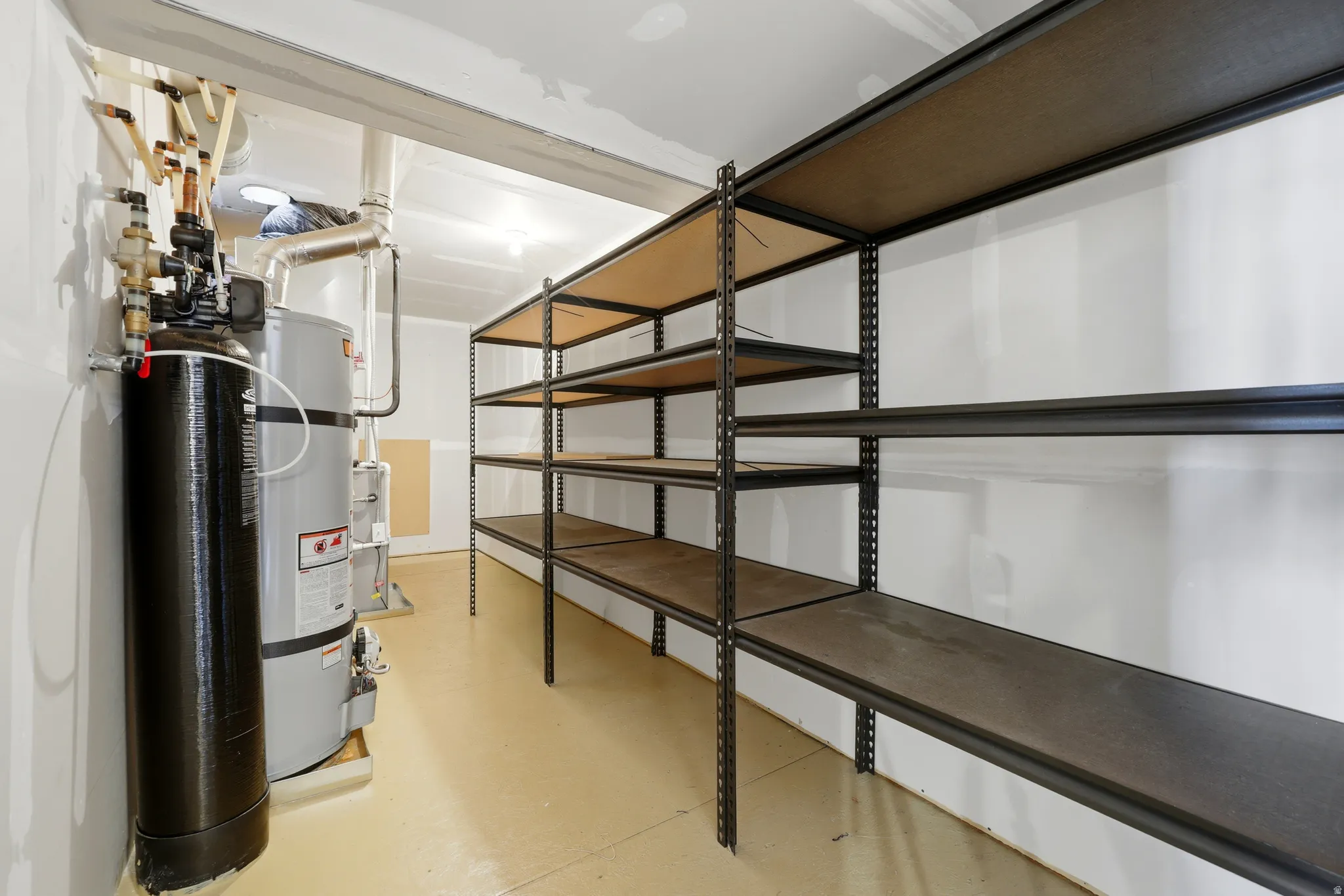 Utility area featuring a water heater, water filtration system, and extensive metal shelving units