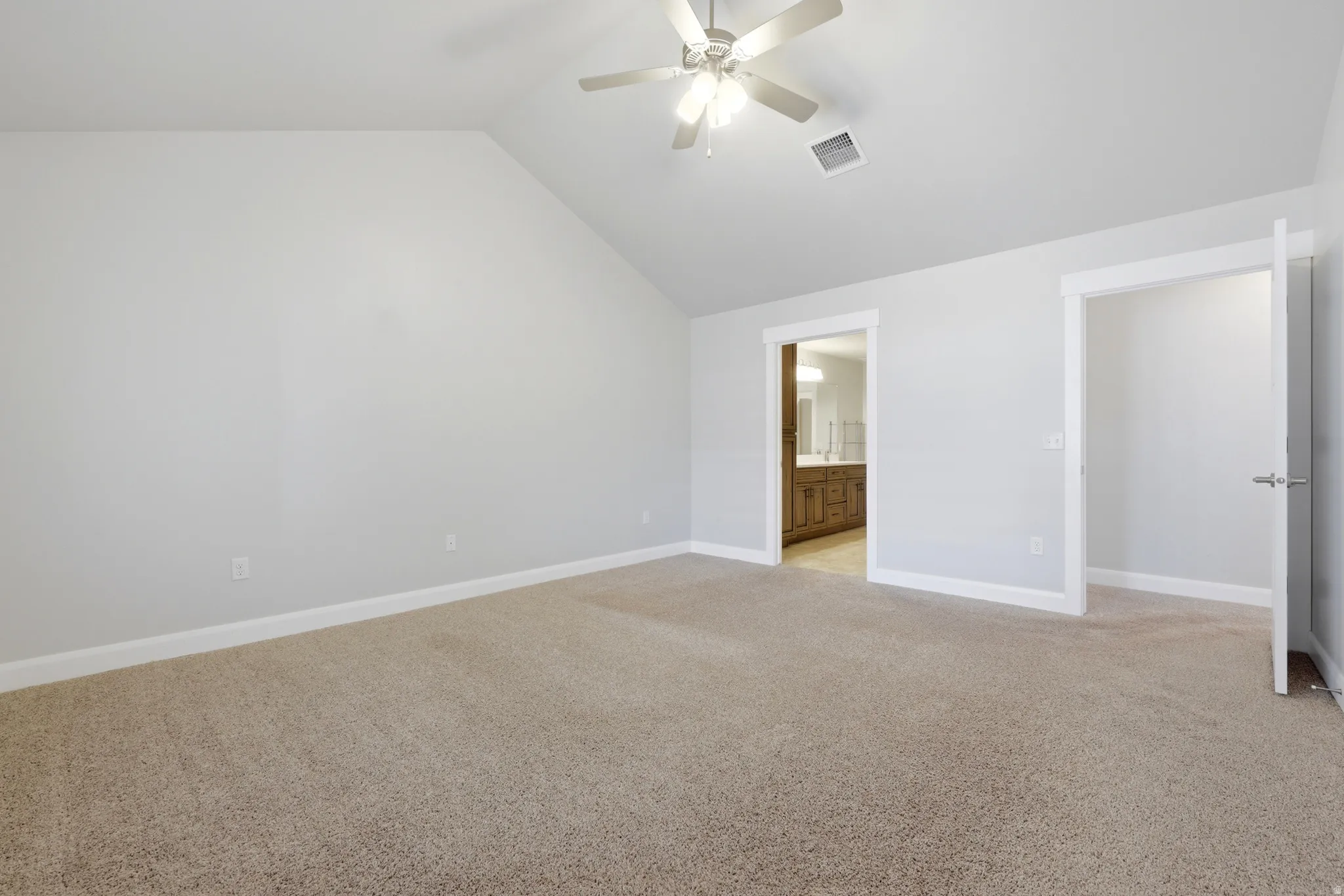 Spacious carpeted room featuring a vaulted ceiling and a ceiling fan