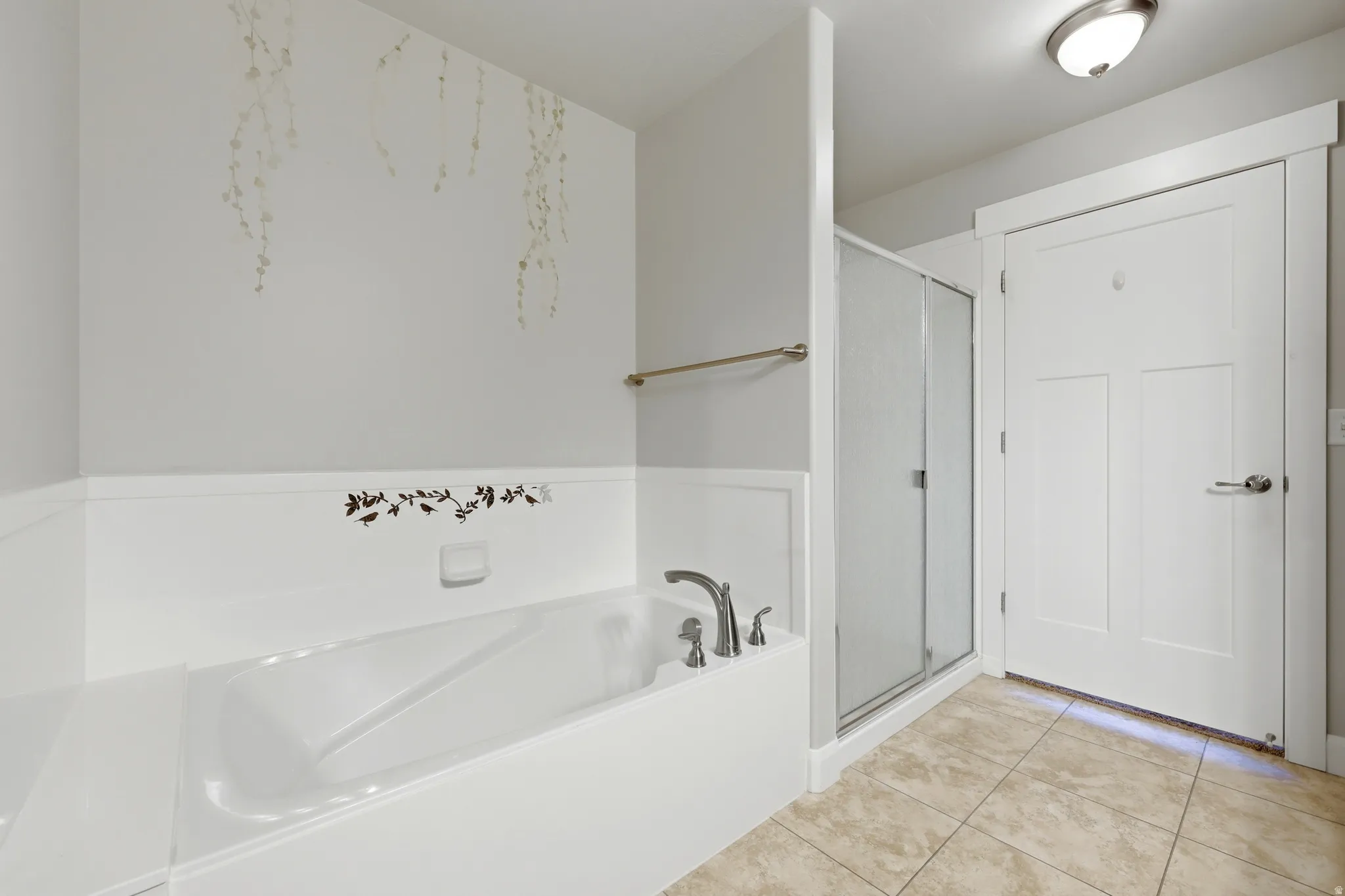 Bathtub and shower combination featuring a built-in tub with deck-mounted fixtures, a glass shower enclosure with a brushed metal frame, and neutral-toned tile flooring