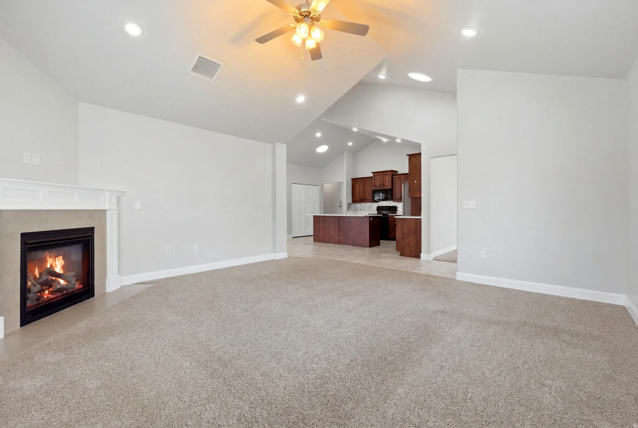 Living area featuring a fireplace with a white mantel, light-toned carpeting, and a ceiling fan