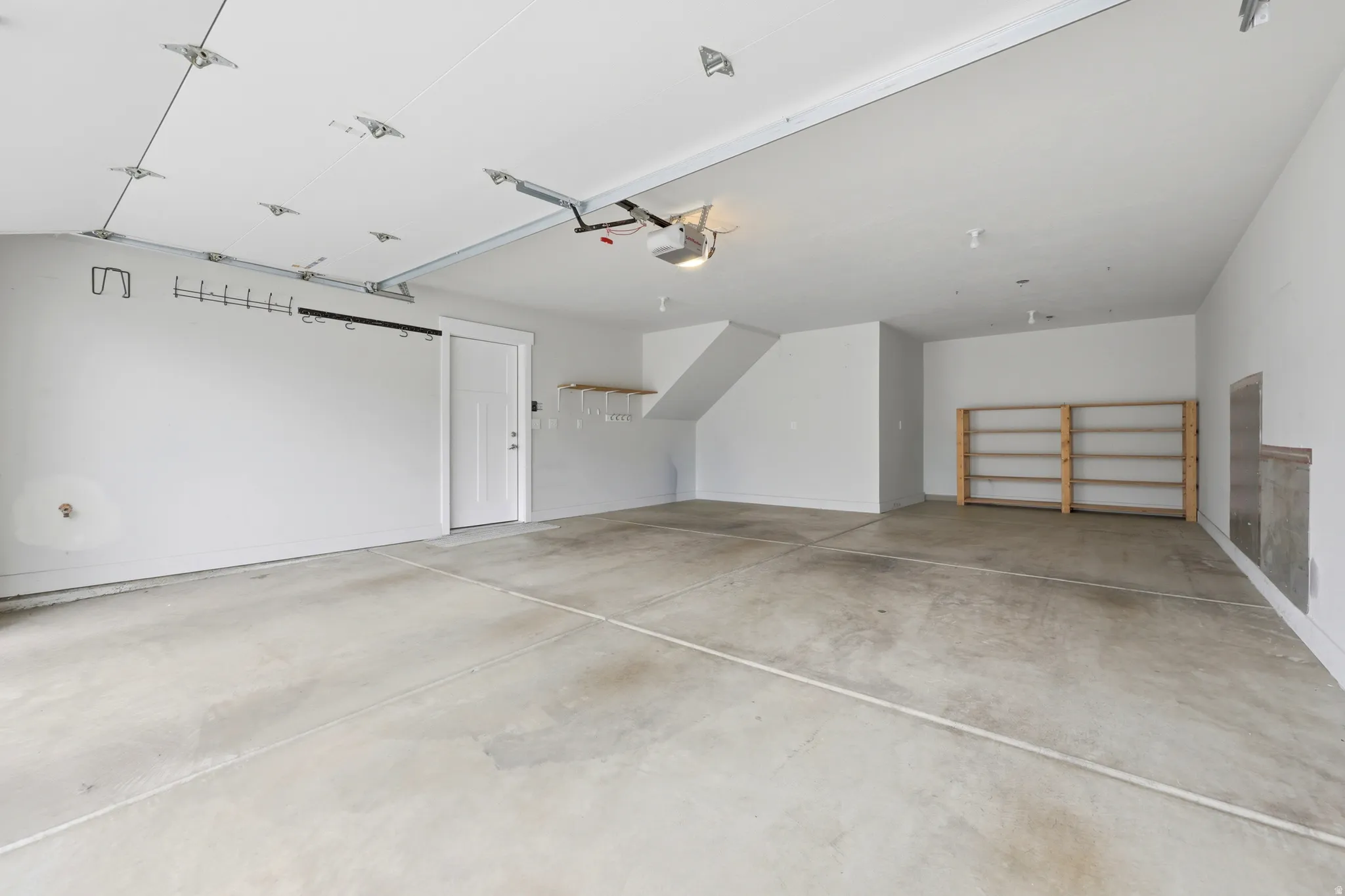 Spacious garage featuring a concrete floor, white painted walls, exposed ceiling tracks, and built-in wooden shelving units