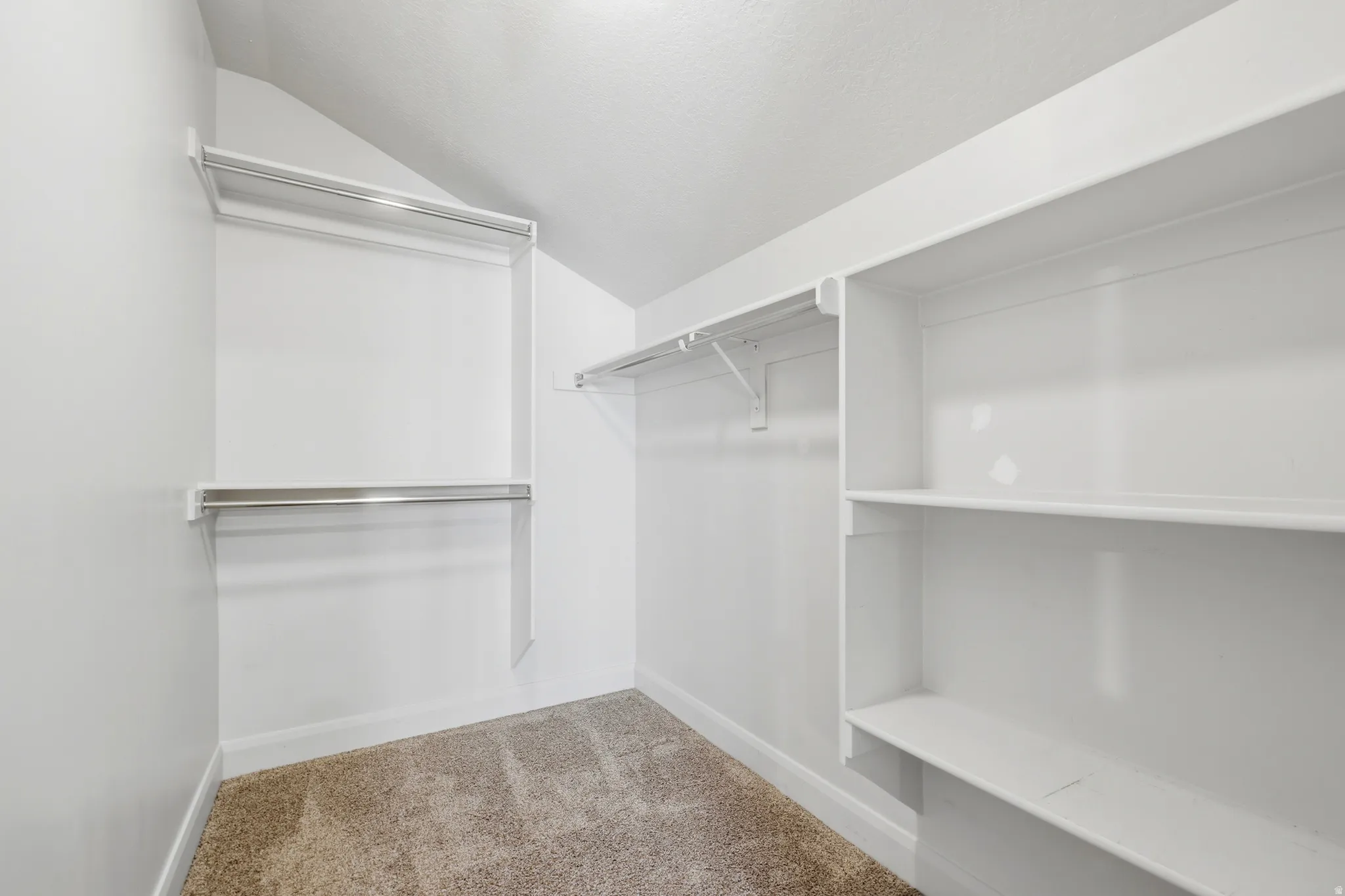 Spacious closet featuring white walls, white shelving, and chrome hanging rods