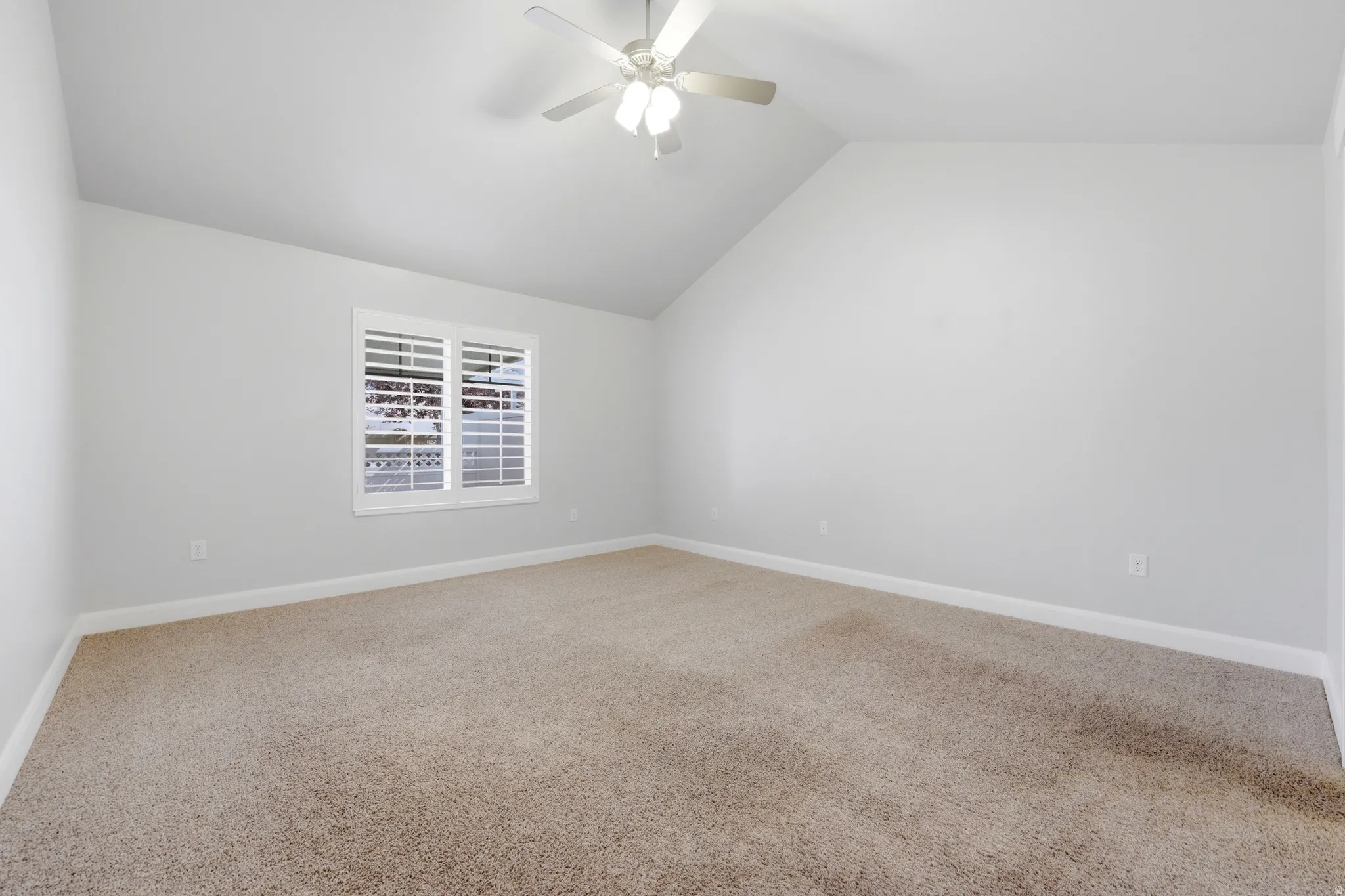Vaulted ceiling with a ceiling fan, neutral carpet flooring, white baseboards, and window with white plantation shutters