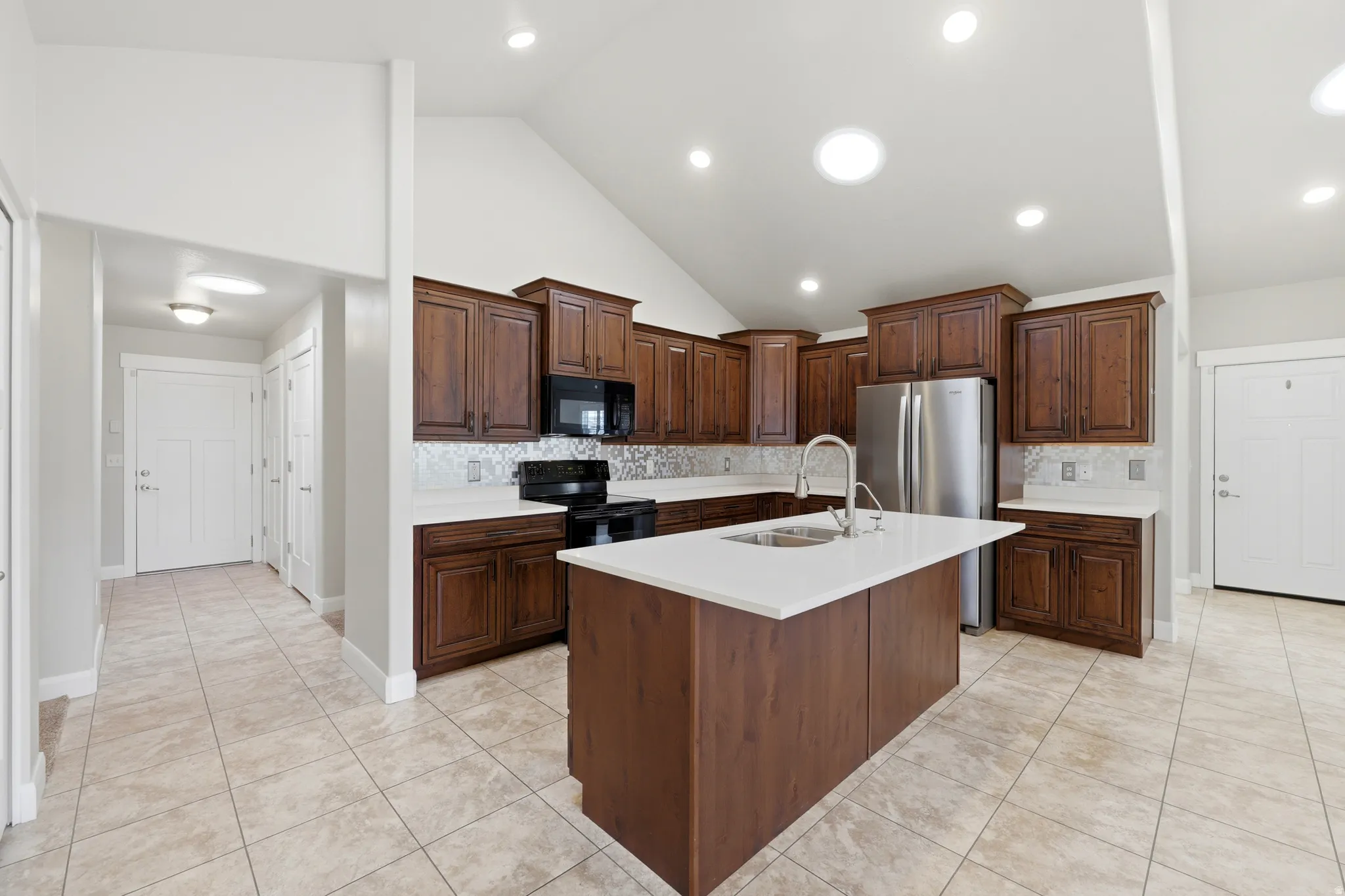 Kitchen with dark wood cabinetry, stainless steel appliances, a center island with a sink, and light-toned countertops