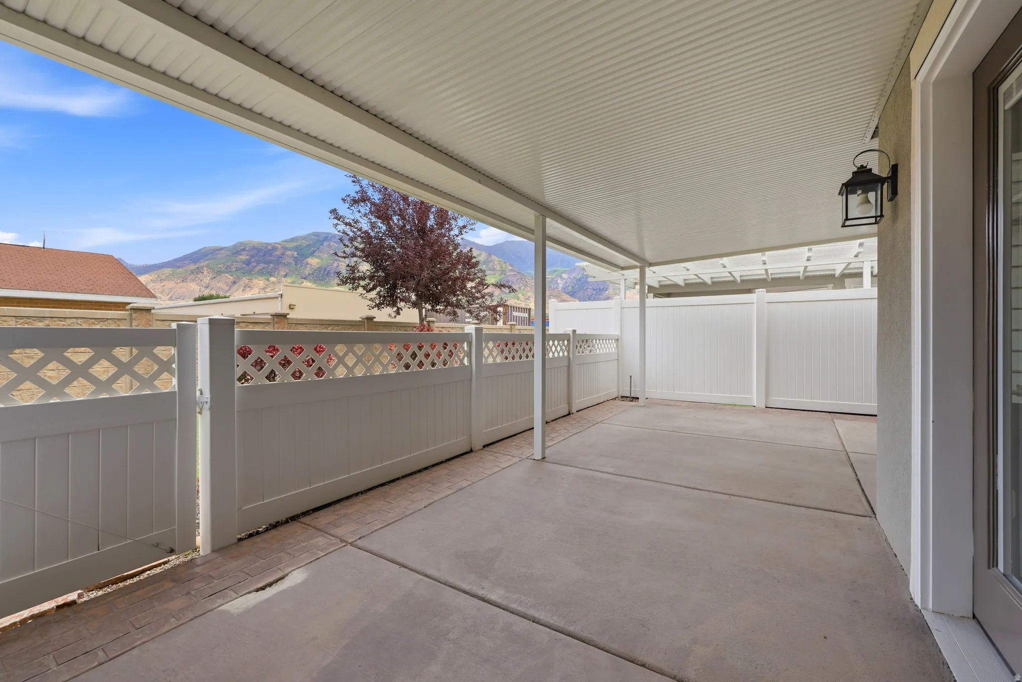 Spacious covered patio featuring a concrete surface, white lattice-top fencing, and a mountain backdrop