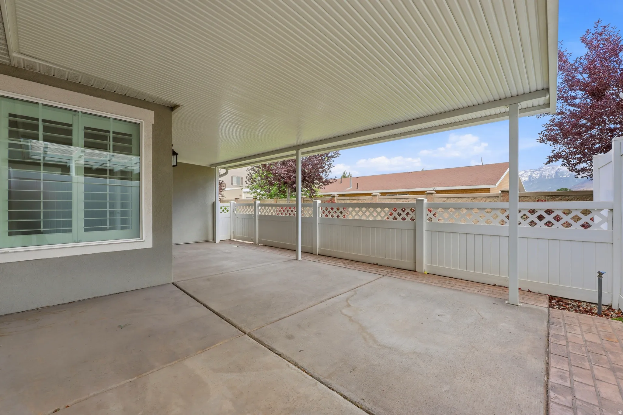 Expansive covered concrete patio with white lattice fencing and an exterior wall lantern