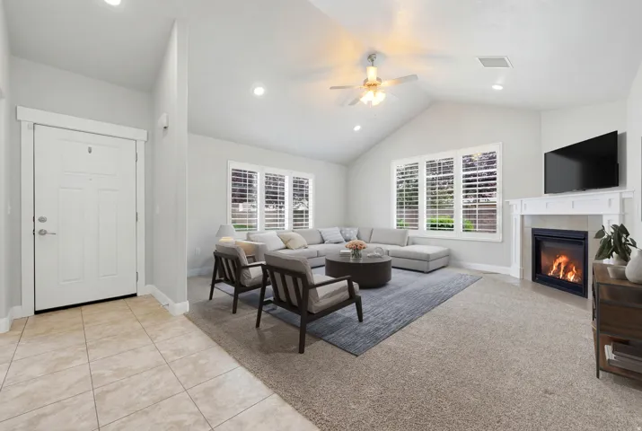 Vaulted ceilings with recessed lighting, fireplace with mantel, ceiling fan, large windows with plantation shutters, and tile entry flooring