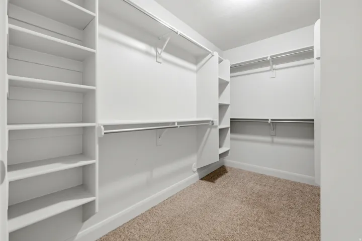Walk-in closet featuring built-in shelving, multiple hanging rods, and neutral carpet flooring