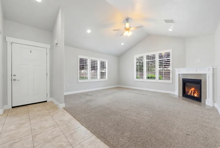 Spacious living area featuring vaulted ceilings, recessed lighting, a ceiling fan, plush carpet flooring, and a corner fireplace with a white mantel