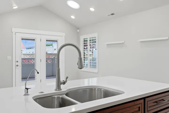 Dual basin stainless steel sink with a high-arch faucet, white countertop, and dark wood-finish cabinetry
