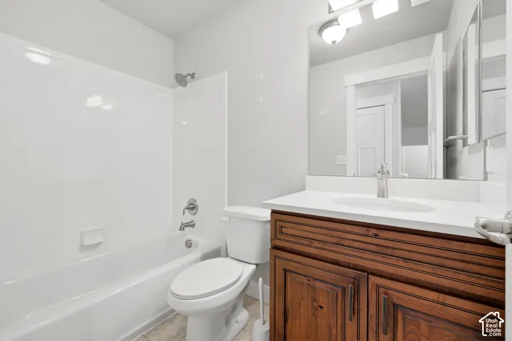 Bathroom featuring a wood-finish vanity with a white countertop, an integrated sink, a large mirror, and a white tub/shower combination