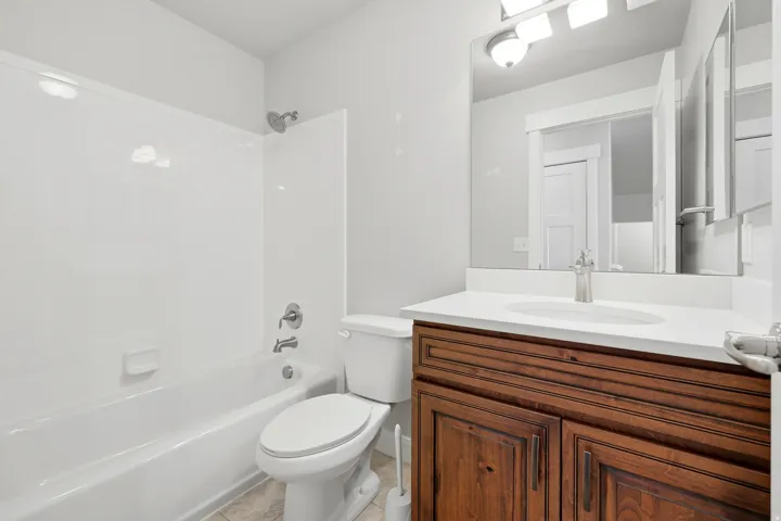 Bathroom featuring a wood-finish vanity with a white countertop, an integrated sink, a large mirror, and a white tub/shower combination