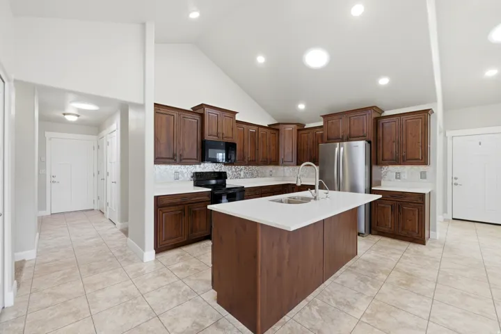 Kitchen with dark wood cabinetry, stainless steel appliances, a center island with a sink, and light-toned countertops