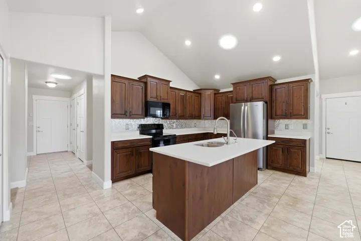 Kitchen with dark wood cabinetry, stainless steel appliances, a center island with a sink, and light-toned countertops