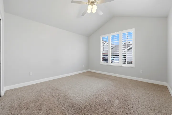 Vaulted ceiling with a ceiling fan, carpeted flooring, and a multiple-pane window with plantation shutters