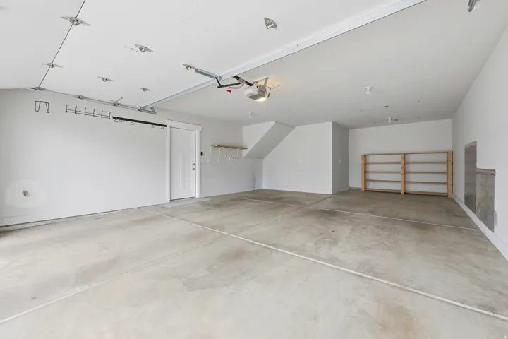 Spacious garage featuring a concrete floor, white painted walls, exposed ceiling tracks, and built-in wooden shelving units