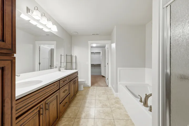 Bathroom featuring a dual vanity with wood cabinetry and white countertops, a built-in bathtub with brushed nickel fixtures, a glass-enclosed shower, and tile flooring