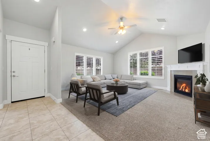 Vaulted ceilings with recessed lighting, fireplace with mantel, ceiling fan, large windows with plantation shutters, and tile entry flooring