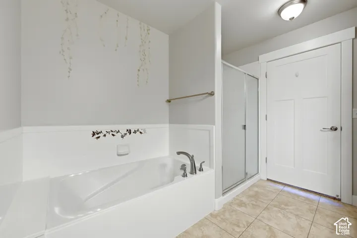 Bathtub and shower combination featuring a built-in tub with deck-mounted fixtures, a glass shower enclosure with a brushed metal frame, and neutral-toned tile flooring