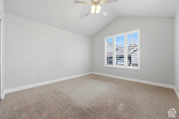 Vaulted ceiling with a ceiling fan, carpeted flooring, and a multiple-pane window with plantation shutters